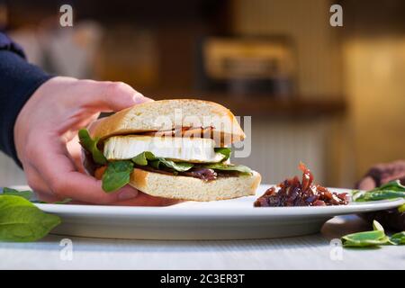 Sandwich Ciabatta avec fromage de chèvre frais, bacon et épinards à la main masculine. Banque D'Images