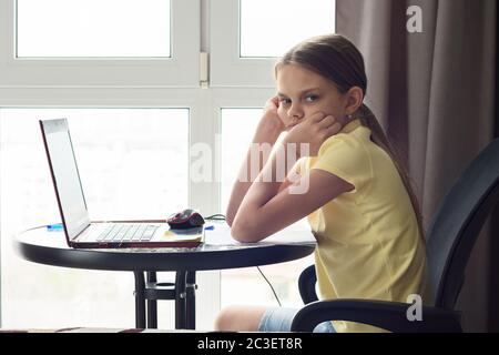 Une jeune fille bouleversée est assise à une table à la maison, fait des devoirs et regarde avec mécontentement Banque D'Images