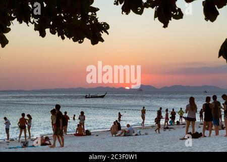 Province de Krabi, Thaïlande - 14 février 2019 : beaucoup de touristes sur la plage de Phra nang profitent de la vue sur le coucher du soleil dans la mer. Sur fond de montagnes, un bateau en bois navigue sur la mer. Banque D'Images