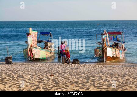 Krabi, Thaïlande - 14 février 2019 : marché flottant. Bateaux alimentaires, comme les chariots de restauration rapide. Vente de fast-food et de boissons à bord des bateaux, Menu à la poupe du navire. L'homme nettoie la plage des ordures Banque D'Images