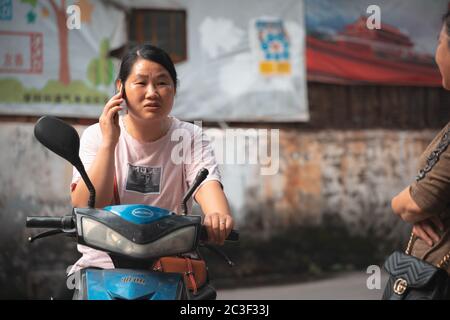 Femme chinoise parlant sur son smartphone sur son scooter Banque D'Images