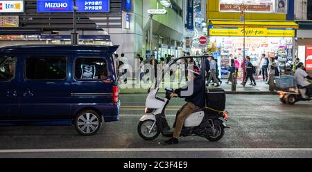 Homme à cheval couvert le cycle automobile dans la rue de Shibuya la nuit, Tokyo, Japon Banque D'Images