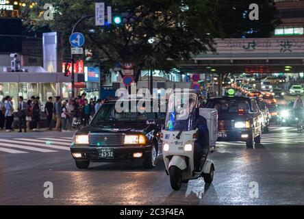 Homme à cheval couvert le cycle automobile dans la rue de Shibuya la nuit, Tokyo, Japon Banque D'Images