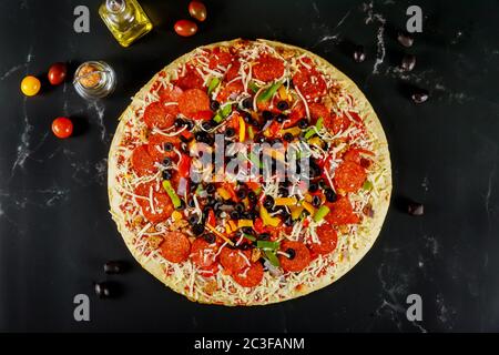 Très grande pizza aux olives, au pepperoni et aux tomates sur fond noir. Banque D'Images