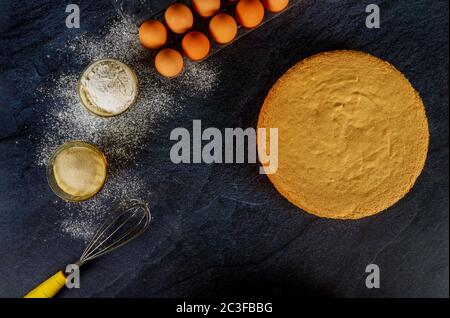 Ingrédients pour gâteau de Savoie. Gâteau rond prêt sur fond noir. Banque D'Images