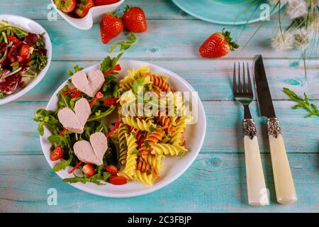 Pâtes de rotini savoureuses de couleur avec saucisses, fraisier frais sur fond bleu en bois. Saint Valentin, dîner pour couple. Banque D'Images