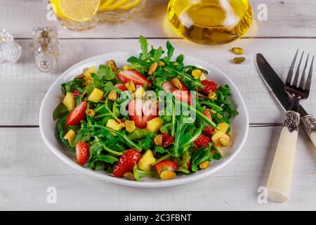 Salade fraîche avec arugula, fraises, ananas et pistaches servie sur une assiette blanche sur une table rustique en bois. Concept organique. Banque D'Images