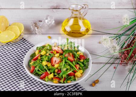 Salade de fraises à l'arugula, à la mangue et aux pistaches avec citron et huile d'olive sur table en bois avec fleurs. Banque D'Images