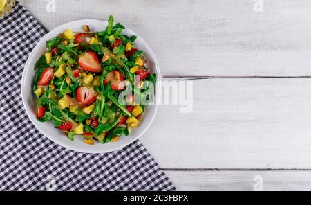 Salade verte avec des arugula fraîches, des fraises et des pistaches sur fond de bois blanc. Banque D'Images
