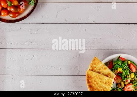 Salade d'arugula fraîche avec fraise, mangue, pistaches et pain pita sur fond de bois blanc. Banque D'Images