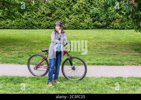 femme enceinte dans un parc avec vélo parlant au téléphone. Banque D'Images