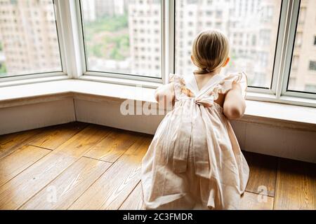 Petite fille élégante avec des cheveux blonds assis à la maison près de la fenêtre pendant l'auto-isolement de covid-19 coronavirus Banque D'Images