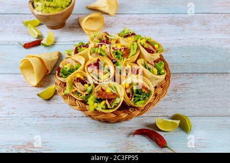 Tortilla fourrées avec fajita sur panier en osier avec lime et guacamole sur table en bois. Banque D'Images