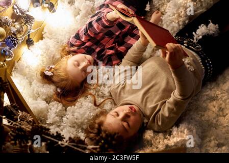 Les enfants lisent un livre dans une salle décorée pour Noël. Banque D'Images