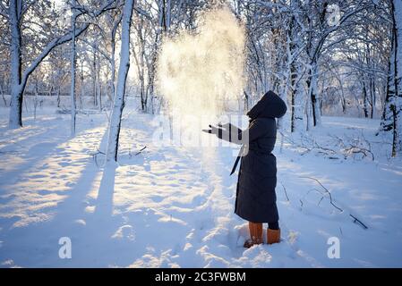 Une jeune femme jette de la neige par temps froid. Jeune femme profitant de l'hiver enneigé. Banque D'Images