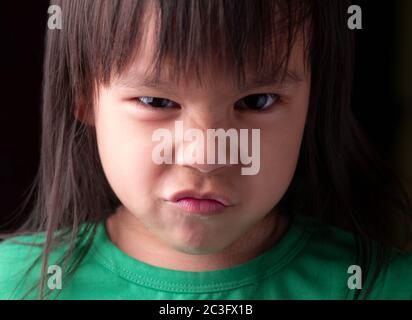 Portrait de la petite fille asiatique avec expression en colère sur fond sombre. Banque D'Images