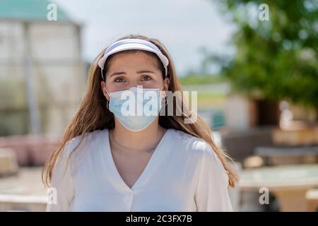 Gros plan d'une jeune femme portant une visière de sport et un masque chirurgical en extérieur sur un arrière-plan flou. Nouveau concept de style de vie et de sécurité. Banque D'Images