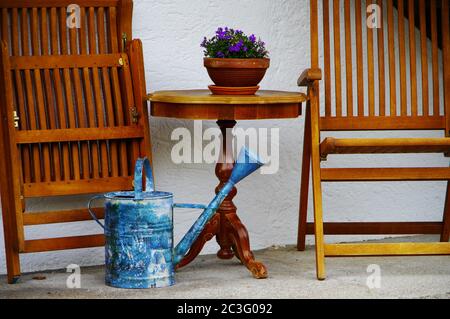 Chaises en bois pliées sur une terrasse avec une table ronde et arrosoir bleu Banque D'Images