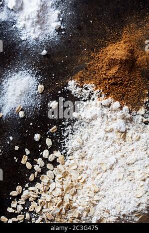 Avoine, cannelle, sel, farine et bicarbonate de soude éparpillés sur fond noir Banque D'Images