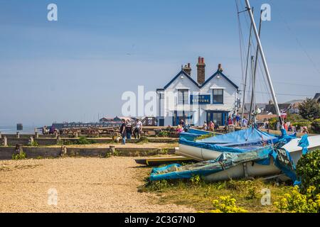 Scène de plage avec pub en bord de mer, les gens qui marchent le long de la plage et les vieux bateaux en bois au premier plan. Prise à Whitstable Bay lors d'un week-end ensoleillé. Banque D'Images