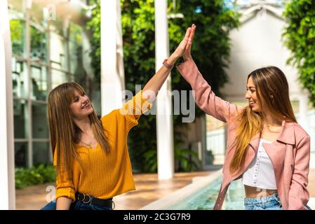 Deux jeunes filles caucasiennes attrayantes avec des cheveux blonds se secouer les mains avec leurs bras dans l'air en souriant à une fontaine à l'intérieur d'une pièce lumineuse avec le Banque D'Images