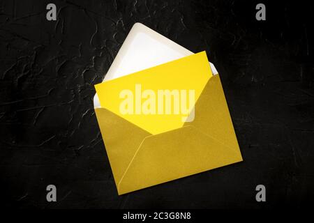 Une carte de vœux jaune dans une maquette d'enveloppe dorée, prise de vue du haut sur un fond noir avec un endroit pour le texte Banque D'Images