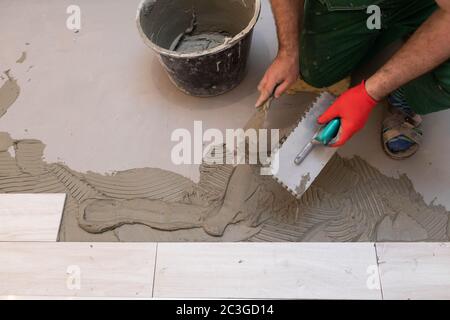 Ouvrier de construction professionnel posant des carreaux de céramique sur le sol dans la salle de bains. Banque D'Images