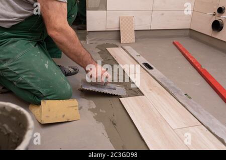 Ouvrier de construction professionnel posant des carreaux de céramique sur le sol dans la salle de bains. Banque D'Images