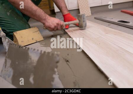 Marteau en caoutchouc. Un ouvrier de construction expérimenté. Terre cuite dans la salle de bains. Vêtements de travail. Il frappe avec un marteau. Banque D'Images