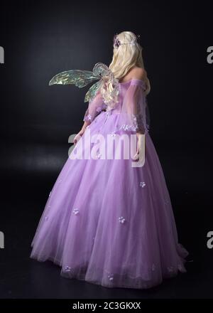 Portrait d'une belle fée blonde portant robe de fantaisie pourpre avec ailes. Posture debout pleine longueur, isolée sur un arrière-plan de studio. Banque D'Images