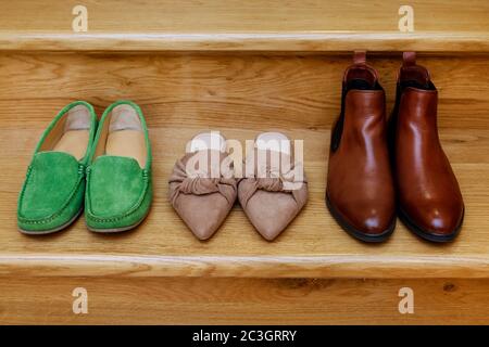 Une paire de mocassins, de mules et de bottines Chelsea sur les escaliers. Image conceptuelle des chaussures de maman, de fille et de père à la maison. Banque D'Images