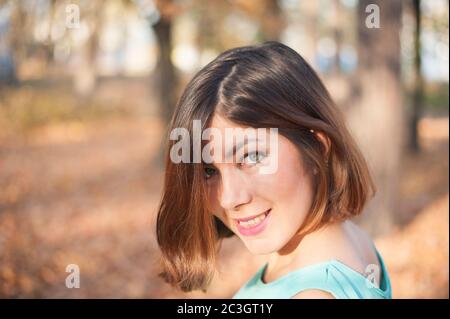 jolie fille aux cheveux sombres et aux sourires bleus, regarde son épaule dans le parc en automne Banque D'Images