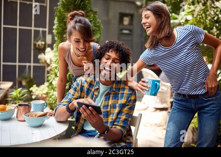 Jeune homme montrant du contenu amusant de mobile à ses amis dans une atmosphère détendue du jardin du café Banque D'Images