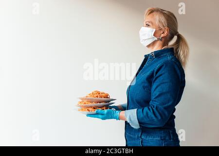 Portrait de femme tenant des assiettes de pâtes italiennes portant un masque chirurgical de protection et des gants en latex - concept de restaurants de livraison de nourriture (restauration rapide) Banque D'Images