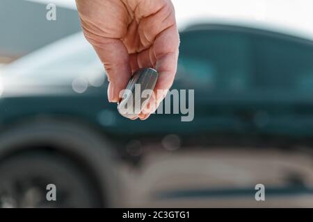 gros plan la main de femme appuie sur un bouton de la télécommande de voiture contre le flou de voiture noire. Banque D'Images