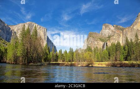 Vue panoramique de la vallée de Yosemite montrant le El Capitan, les Cathedral Rocks et les chutes de Bridalveil, avec la rivière Merced en premier plan et le ciel bleu W Banque D'Images