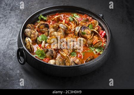 Coque de tapis japonais cuite avec paprika et herbes dans une sauce à l'ail épicée de tomate comme un gros plan dans une casserole moderne Banque D'Images