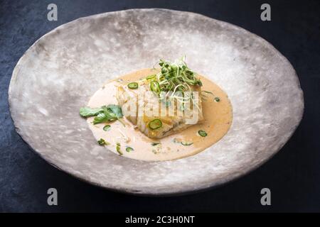 Poisson frit gastronomique à la morue au curry thaïlandais avec piment et pousses, à l'aide d'une assiette moderne avec espace pour les copies Banque D'Images