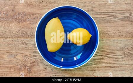 fruits jaunes - citron et mangue - sur une assiette bleue sur un plan d'examen en bois Banque D'Images