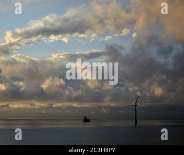 Aube vue de la côte, ciel nuageux et éolienne marine avec mer calme Banque D'Images