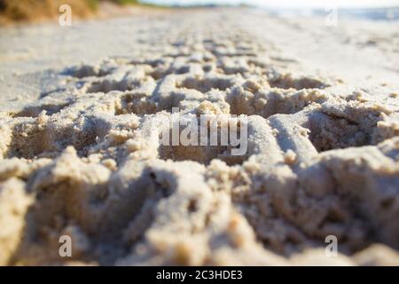 Empreinte dans le sable d'un pneu de voiture ou quadro cycle au lever du soleil sur un fond bleu ciel et mer, horizon plage aube Banque D'Images