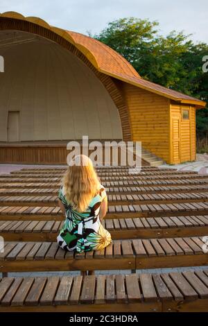 La fille est assise seule dans son dos parmi les nombreux bancs du théâtre de rue Banque D'Images