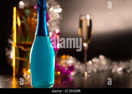 Concept fête, nouvel an ou Noël avec bouteille de champagne bleue colorée devant une flûte de vin mousseux et des décorations scintillantes colorées Banque D'Images