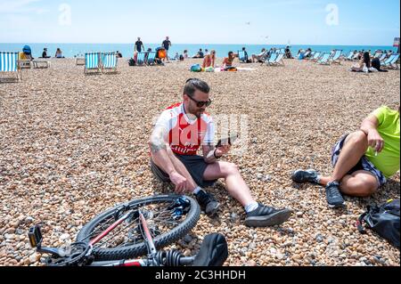 Brighton UK 20 juin 2020 - un fan de football d'Arsenal se fait écouter sur son téléphone mobile sur Brighton Beach pour assister aujourd'hui au match de la Premier League contre Brighton lors de la crise pandémique du coronavirus COVID-19 . Tous les matches sont joués derrière des portes fermées en raison des restrictions de verrouillage : crédit Simon Dack / Alamy Live News Banque D'Images