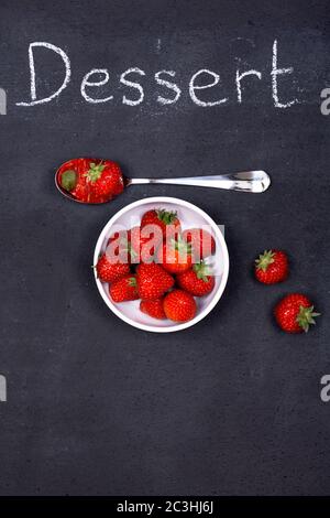 Un bol de fraises fraîches mûres avec une cuillère sur un tableau à craie, comme spécial de la journée. Banque D'Images