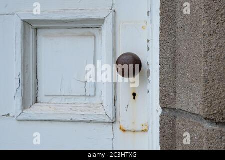 Porte vintage peinte en blanc avec un accent sur le bouton de porte et le trou de serrure. Il y a de la rouille sur les meubles métalliques de la porte. Un mur de briques est adjacent à la porte. Banque D'Images