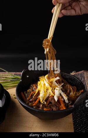 Cliché vertical d'une personne tenant des nouilles de verre cuites avec baguettes en bois sous les feux Banque D'Images