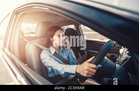 Les femmes d'affaires discutent avec le client par téléphone et conduisent la voiture sur la route dans la ville. Banque D'Images