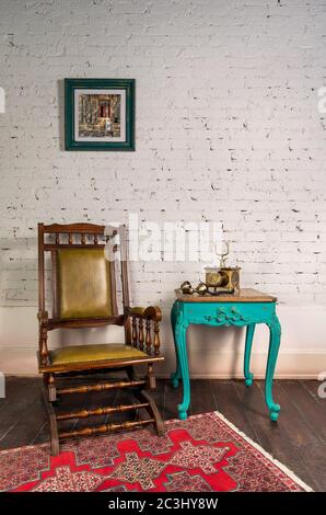 Fauteuil à bascule classique en bois, téléphone ancien doré sur table en bois vert vintage et fond de mur en briques blanches avec peinture pendu et parquet avec moquette rouge Banque D'Images