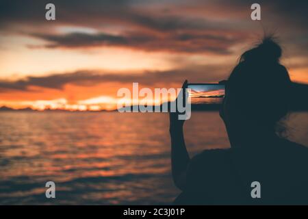 silhouette femmes utilisent un téléphone mobile pour prendre un paysage marin avec le coucher du soleil. Banque D'Images